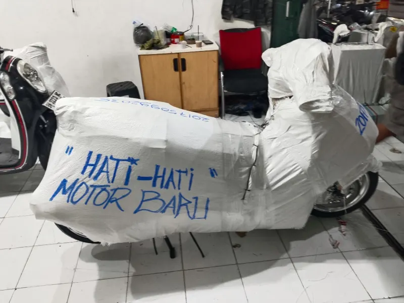 Motor dibungkus karung dengan label Hati-hati Motor Baru, siap dikirim